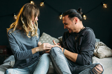 Young couple sitting on bed and laughing while tickling each other. Smiling happy people. Curly...