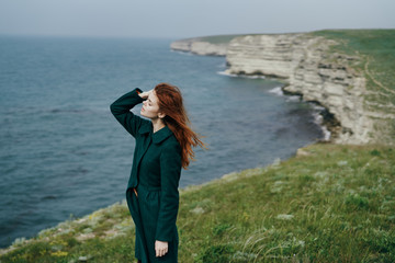 Beautiful young woman standing on a cliff above the sea, mountains, nature