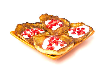 Fritters on a white background on a plate. Pancakes on an orange plate with sour cream, jam and pomegranate.