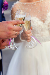 Hands of bride and groom clink glasses with champagne