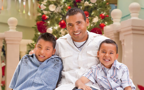 Hispanic Young Father And Sons In Front Of Decorated Christmas Tree.