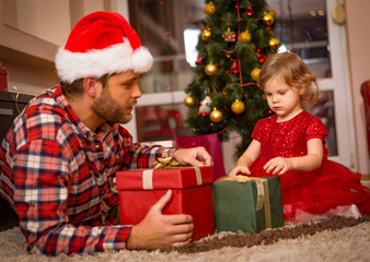 Fototapeta na wymiar family, christmas, x-mas, happiness and people concept - smiling father and daughter in santa helper hats holding gift box