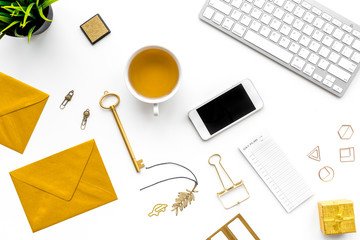 Fashoin in the workplace. Office desk in a trendy gold color. Stationery near keyboard and cell phone on white background top view