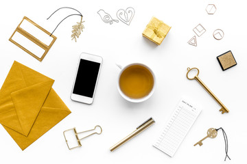 Office desk in trendy gold color. Glittering stationery near cup of tea, cell phone   on white background top view