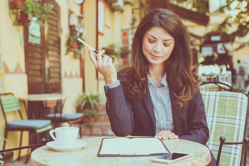 Smiling business woman writing papers at cafe.