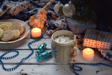 Christmas and new year holiday celebration concept background. Cup of cocoa with marshmallow, homemade chocolate cookie and peanut biscuit, lighted candles, xmas tree decoration on wooden table.