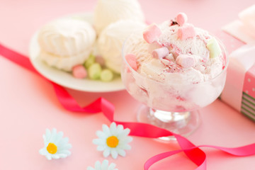 Fototapeta na wymiar ice cream in a Cup next to the marshmallows, flowers, pink sweets