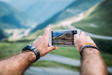 Hands holding a phone and photographing the mountains