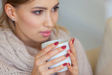 Beautiful woman holding a cup of coffee in her hands. in a knitted beige sweater