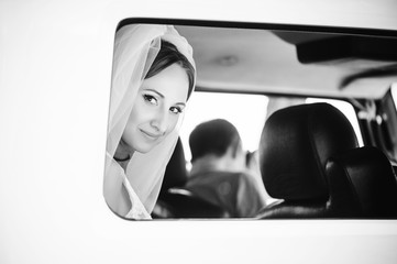 tender happy bride in the car, happy woman in a wedding dress looking out the window, white veil on her head, contrasting black and white