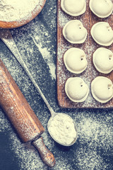 Raw dumplings on a black background, flour, rolling pin, spoon, vertically, flat lay