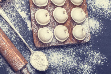 Raw dumplings on a black background, flour, rolling pin, spoon, horizontally, flat lay