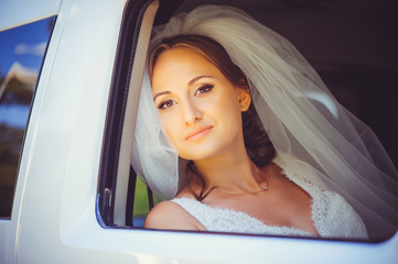 tender happy bride in the car, happy woman in a wedding dress looking out the window, white veil on...