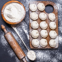 Raw dumplings on a black background, flour, rolling pin, spoon, flat lay, square