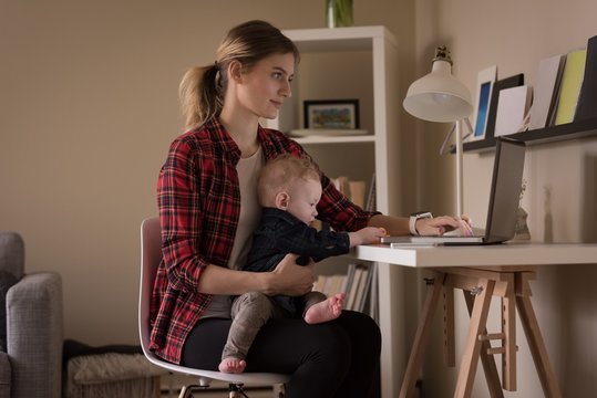 Young woman using laptop computer while sitting with son
