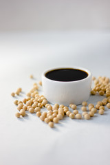 Soybean sauce surrounded by soy beans over white background.