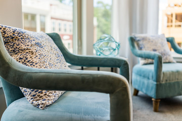 Closeup of two new modern blue couch chairs by windows with natural light and pillows