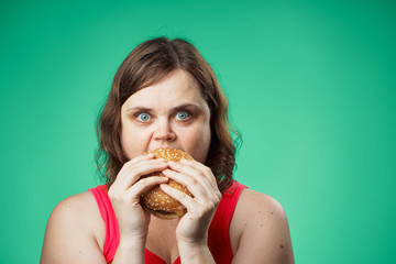 Fat woman on a green background eating a hamburger, fast food