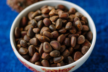 Fresh and ripe pine or cedar nuts in a bowl over blue background.