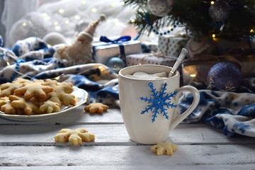 Christmas and new year holiday celebration concept background. Cup of cocoa with marshmallow, homemade chocolate cookie and peanut biscuit, lighted candles, xmas tree decoration on wooden table.