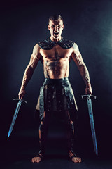 Portrait of handsome muscular gladiator with two swords. Studio shot. Black background. Scream.