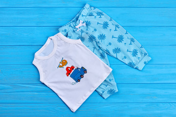 Baby summer fashion style clothes. Baby boy organic t-shirt and printed pants on blue wooden surface, top view.