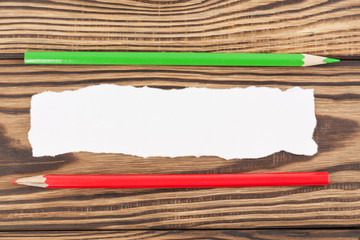 Two pencils red and green color near torn white blank paper on old wooden brown table