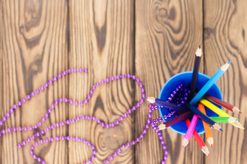 Lot of colored pencils in blue plastic glass and violet glossy beads on old wooden brown table