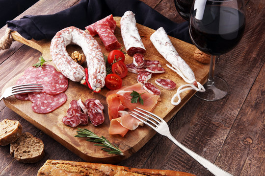 Wooden cutting board with prosciutto, salami, sausages, wine, bread  and  rosemary