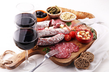 Italian antipasti wine snacks variety set. Cheese, Mediterranean olives, pickles, Prosciutto di Parma, tomatoes, artichokes and wine in glasses. Spanish tapas.