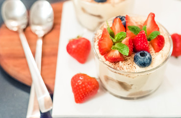 Homemade italian dessert tiramisu with strawberrie, blueberry, mint in glass jars, top view on a white background