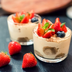Homemade italian dessert tiramisu with strawberries, mint and blueberry in glass