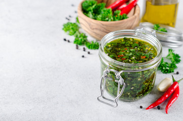 Traditional argentinian chimichurri sauce made of parsley, cilantro, garlic and chili pepper in a glass jar. Selective focus, horizontal image