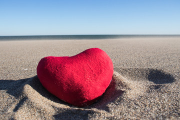 Red plush heart on the sand under the scorching sun.