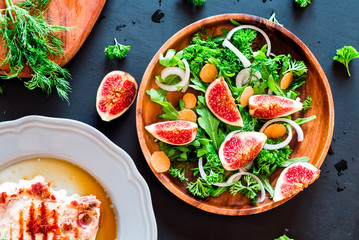 Autumn salad of arugula, figs in a brown earthenware plate on a dark background. top view