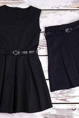 Black belted dress and skirt. School girl classic pleated black dress and skirt on old wooden background, top view.