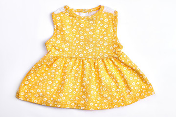 Baby-girl yellow patterned top. Newborn baby girl cotton sleeveless dress with a pattern of small white flowers, white background. Infant girl summer clothes.