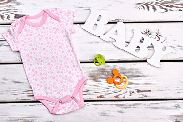 Baby-girl clothes and accessories. Newborn baby-girl cute organic printed bodysuit, teether, pacifier on old wooden background, top view.