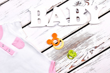 Baby-girl summer bodysuit with pocket. High quality organic clothes for newborn kids, toy, pacifier, old wooden background.