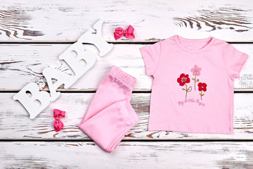 Baby-girl cotton summer suit. Little girl beautiful pink leggings, cartoon t-shirt, hair bows, old wooden background.