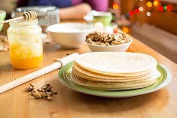 Christmas wafers placed on a wooden kitchen table, on a green plate next to a window. Wafers are round, cream color, surrounded by ingredients