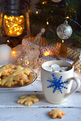 Christmas and new year holiday celebration concept background. Cup of cocoa with marshmallow, homemade chocolate cookie and peanut biscuit, lighted candles, xmas tree decoration on wooden table.