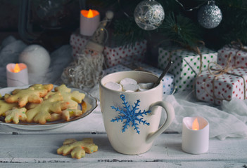 Christmas and new year holiday celebration concept background. Cup of cocoa with marshmallow, homemade chocolate cookie and peanut biscuit, lighted candles, xmas tree decoration on wooden table.