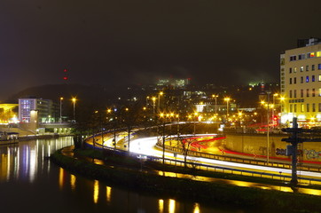 Fototapeta na wymiar Saarbrücken Stadtautobahn bei Nacht in Deutschland mit fließenden Autolichtern und Hochhäusern im Hintergrund