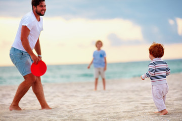 happy father with kids, family playing flying disc golf on evening beach