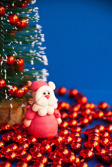 Merry Christmas greeting card with santa claus toy, christmas tree and red garland on blue background in macro