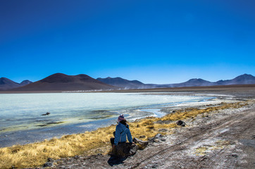 Fototapeta na wymiar Girl seatting on the Laguna Verde is a salt lake at the foot of the volcanos Licancabur and Juriques - Eduardo Avaroa Andean Fauna National Reserve, Bolivia