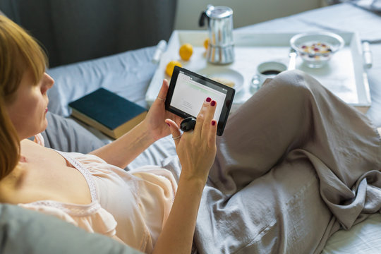 Breakfast and morning news- women reading morning  news on her tablet in bed