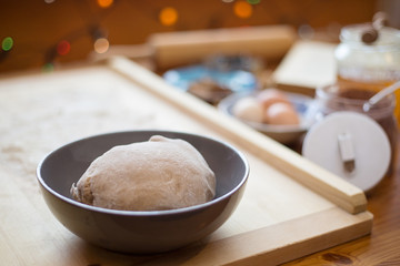 Ginger bread dough placed inside a round deep plate, in the kitchen, on a wooden table.  Ingredients at the background, christmas baking at home concept. Selective focus