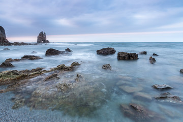 sunset at the beach of Portizuelo, asturias, with its large rock in the shape of a mask in the background and the sea with silk effect